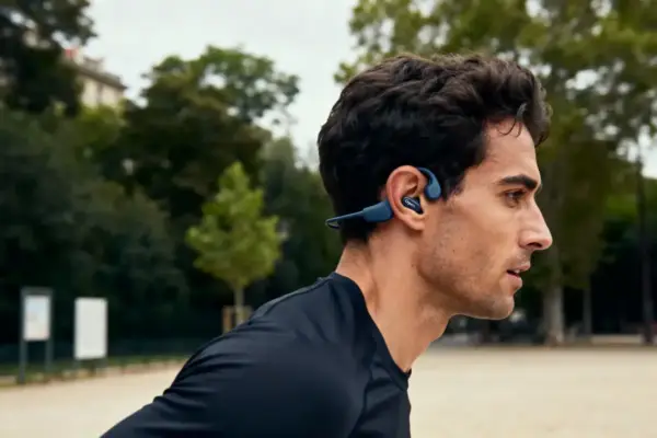 Homme courant dans un parc, portant un casque audio bleu. Fond arboré flou.