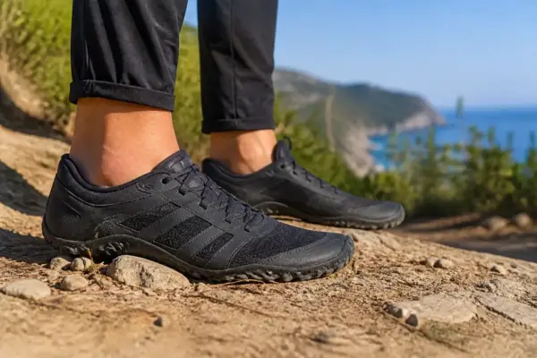 Personne portant des chaussures minimalistes noires sur un sentier de randonnée côtier ensoleillé