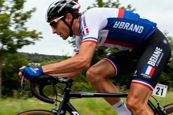 Cycliste en tenue française lors d'une course, concentré sur son vélo, fond de campagne verdoyante floue.