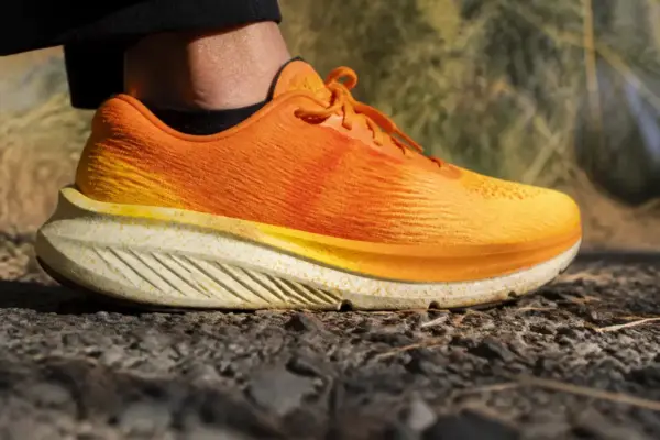 Chaussure de running orange avec faible drop sur chemin caillouteux en extérieur.