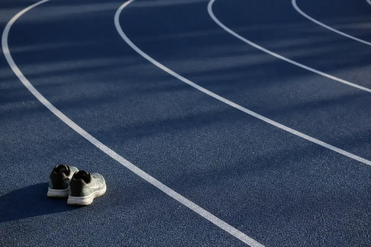 Couloirs d’une piste d’athlétisme bleu nuit dans le virage, une paire de chaussures de course posée au bord